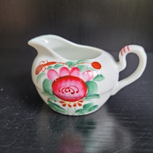 Sahnekännchen, weiß, mit Pink farbener Blüte und grünen Blättern