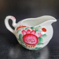 Sahnekännchen, weiß, mit Pink farbener Blüte und grünen Blättern
