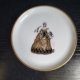 Kleiner Teller, weiß, mit Goldrand. Motiv: Frau mit langem goldenen Kleid
