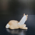 Liegendes Pferd in hellbeige und weiß. Rückansicht