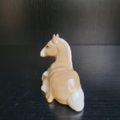 Liegendes Pferd in hellbeige und weiß. Ansicht von hinten